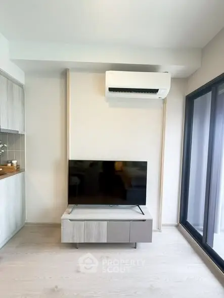 Modern living room with sleek TV setup and air conditioning, featuring large windows for natural light.