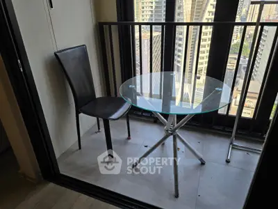 Modern balcony with glass table and chair offering city view in high-rise apartment.