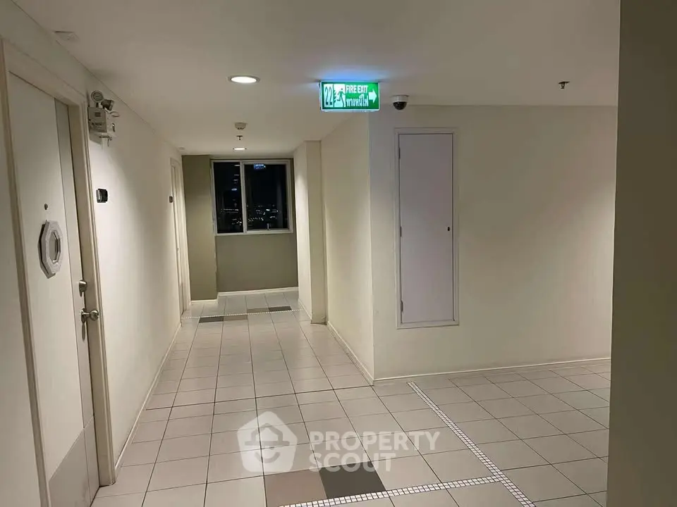 Modern apartment corridor with emergency exit sign and tiled flooring.