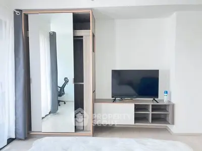 Modern bedroom with sleek wardrobe and TV unit, featuring a glimpse of a stylish office chair.