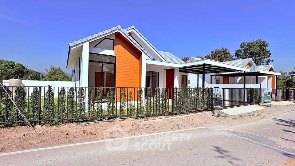 Modern single-story house with vibrant orange facade and sleek metal fence under clear blue sky.