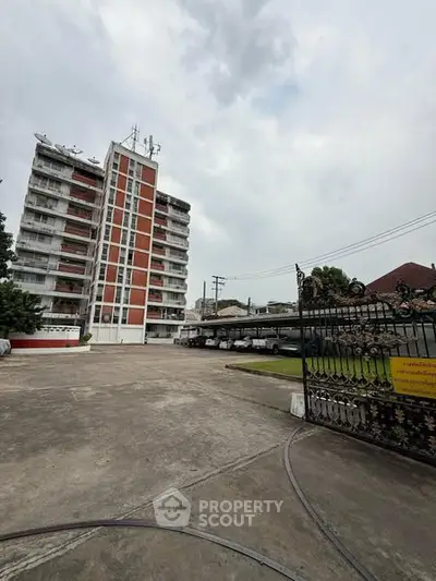 Modern apartment building with spacious parking area and secure entrance gate.