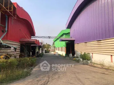 Colorful industrial warehouses with vibrant red, green, and purple exteriors on a sunny day.