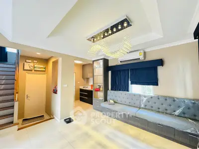 Modern living room with elegant chandelier and built-in seating, featuring a cozy staircase and stylish decor.