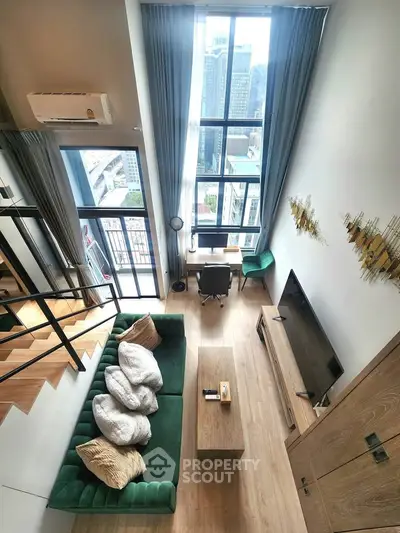 Modern loft-style living room with high ceilings and city view, featuring a green sofa and stylish decor.
