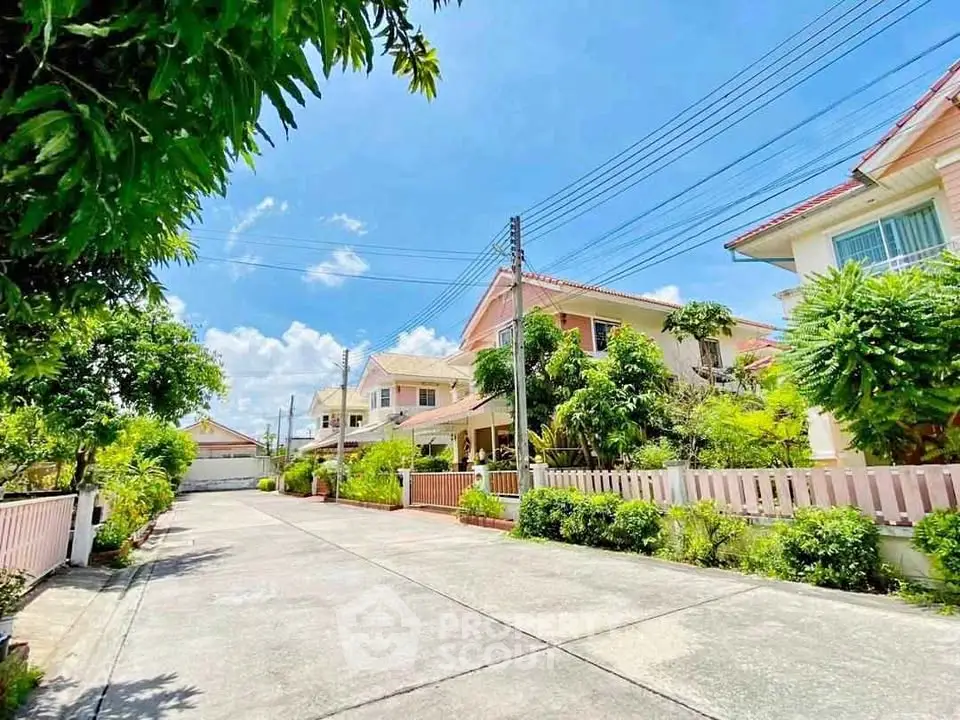 Charming suburban street with beautiful houses and lush greenery under a clear blue sky.