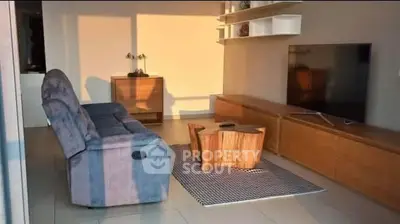 Modern living room with stylish furniture and large TV, bathed in warm sunlight.