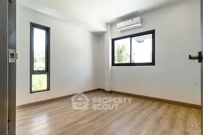 Spacious empty room with wooden flooring and large windows in modern apartment.
