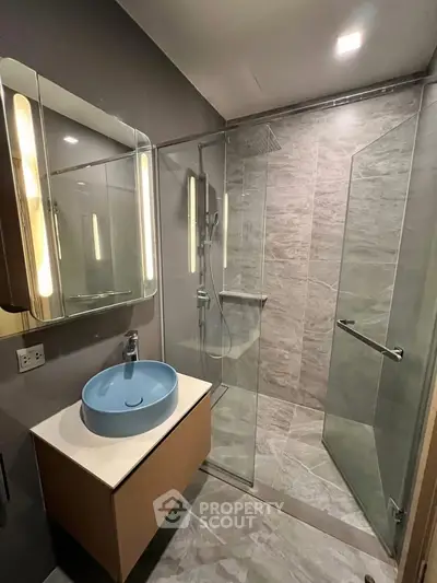 Modern bathroom with glass shower and stylish blue basin in sleek design.