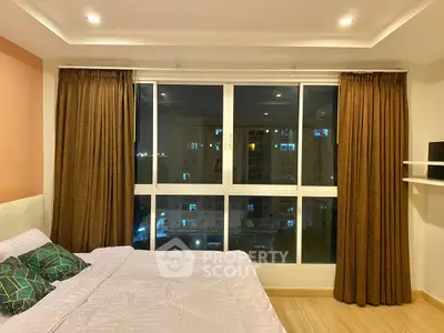 Cozy bedroom with large window offering city view, warm lighting, and elegant curtains.