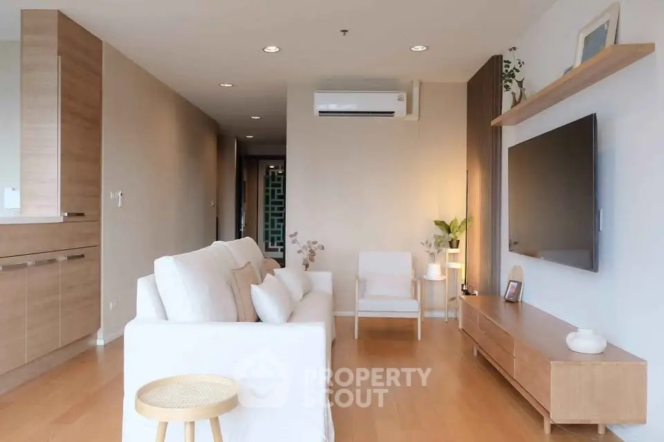 Modern living room with sleek furniture and wall-mounted TV, featuring warm wooden flooring and neutral tones.