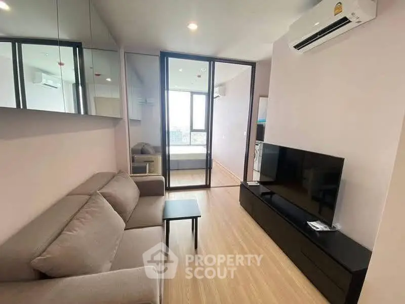 Modern living room with sleek furniture and large TV, featuring a view into a cozy bedroom.