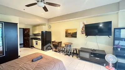 Spacious studio apartment with modern amenities and stylish decor, featuring a cozy bed, flat-screen TV, and ceiling fan.
