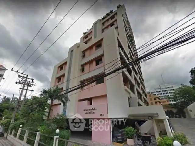 Modern multi-story residential building with lush greenery and overcast sky.
