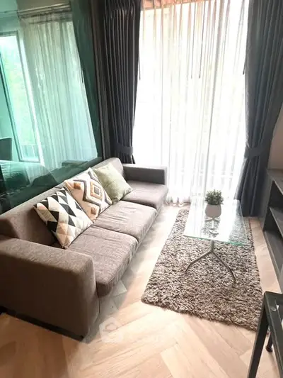 Stylish living room with modern sofa and glass coffee table, featuring elegant curtains and cozy decor.