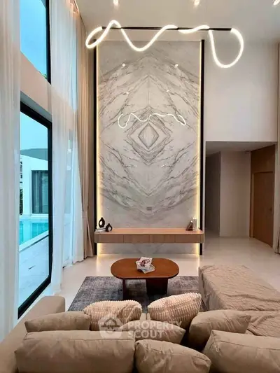 Luxurious living room with high ceilings and modern lighting, overlooking a pool through large windows.