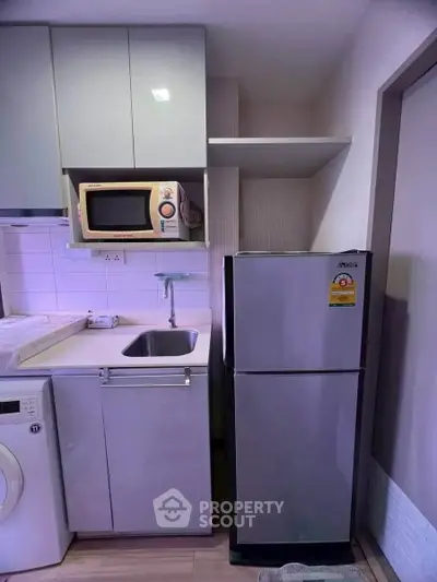 Compact modern kitchen with fridge, microwave, and washing machine in a sleek apartment.