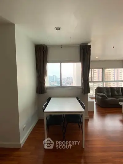 Spacious living room with city view, wooden flooring, and modern furniture in a high-rise apartment.