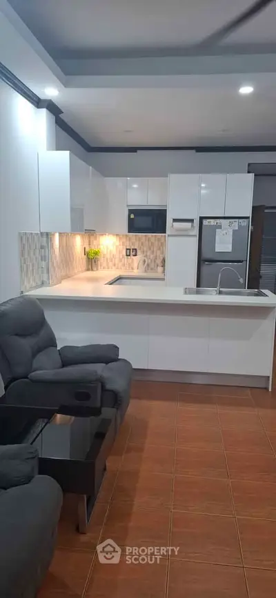 Modern open-layout kitchen with sleek white cabinets and cozy living area.