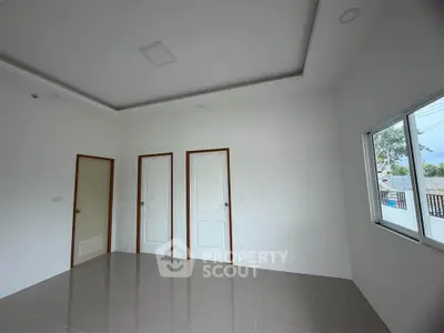 Spacious empty room with tiled floor and large window, ideal for customization.