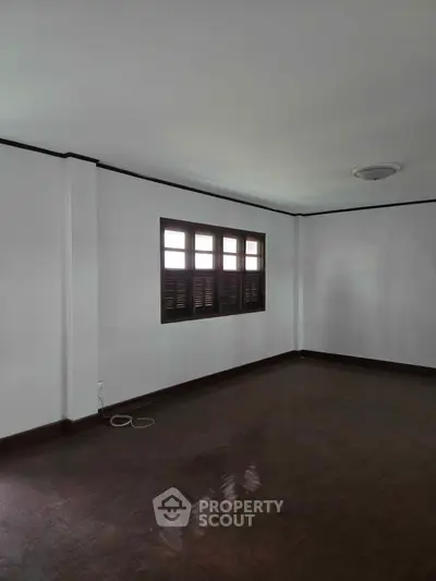 Spacious empty room with wooden flooring and large window, ideal for customization.