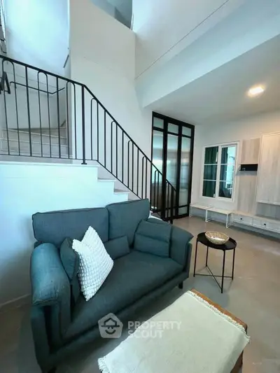 Modern living room with stylish sofa and elegant staircase in a bright, open space.
