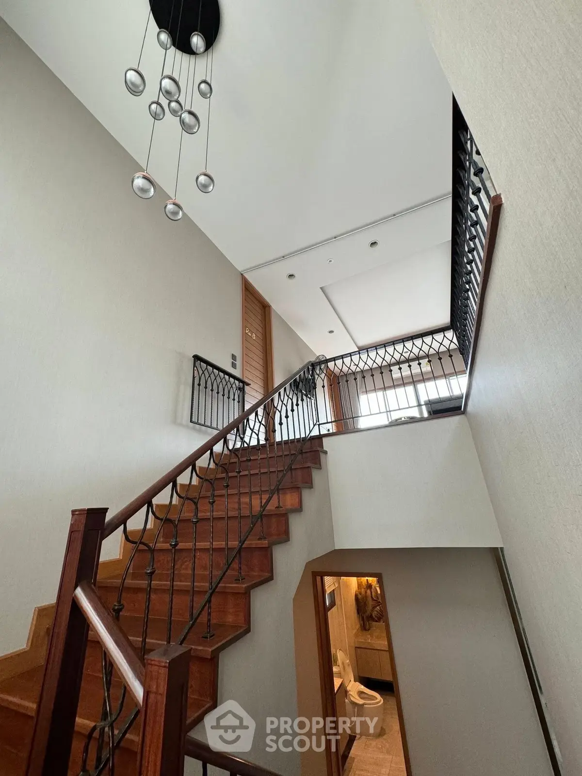 Elegant staircase with modern chandelier and sleek railing in a stylish home interior.