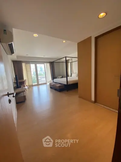 Spacious bedroom with large windows and balcony access in modern apartment.