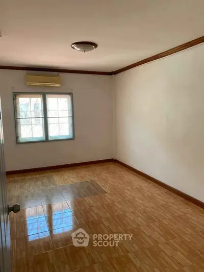 Spacious empty room with wooden flooring and large window, perfect for customization.