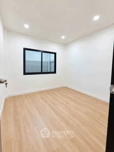 Spacious empty room with wooden flooring and large window, perfect for customization.