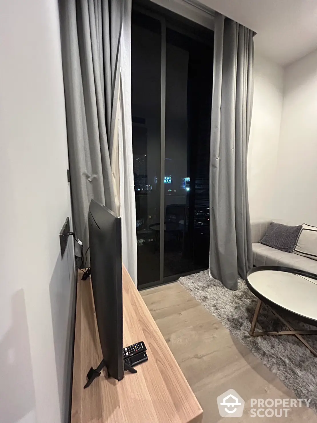 Modern living room with sleek furnishings, plush rug, and floor-to-ceiling windows offering a glimpse of the city's night lights.