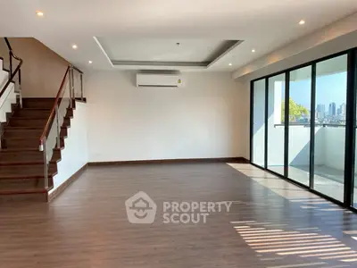 Spacious modern living room with large windows and city view, featuring wooden flooring and elegant staircase.