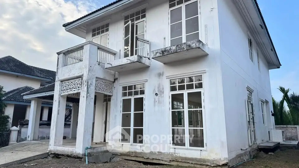 Spacious two-story white house with large windows and balcony, ideal for renovation.