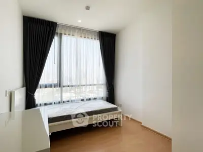 Bright minimalist bedroom with large window and city view, featuring sleek furnishings and modern design.