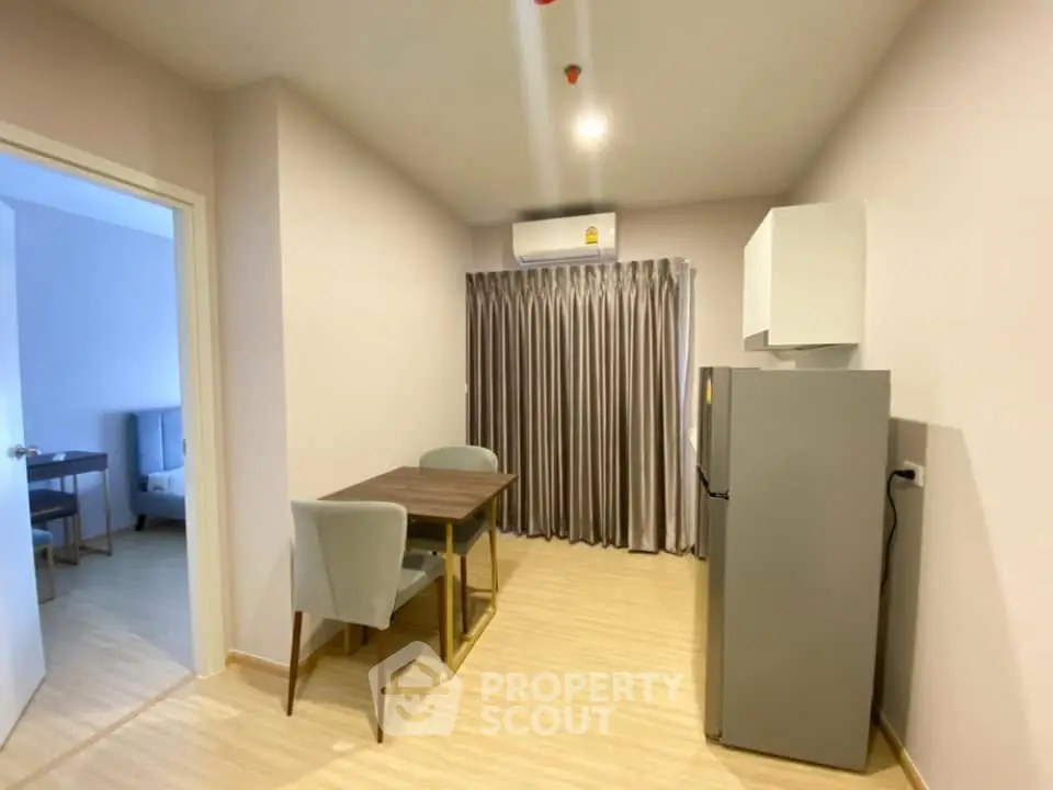 Modern dining area with sleek table and chairs, adjacent to a compact kitchen with fridge and air conditioning.