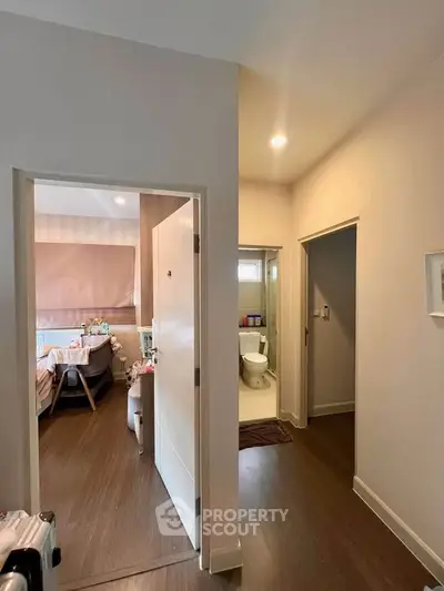 Modern apartment hallway with view into bedroom and bathroom, featuring sleek wood flooring.