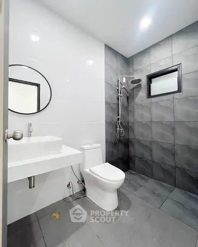 Modern bathroom with sleek design, featuring a round mirror, white sink, and contemporary shower area.