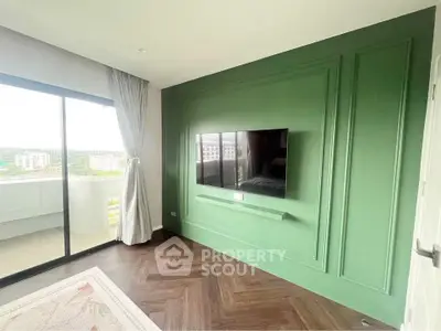 Modern living room with green accent wall and large TV, featuring a balcony with scenic view.