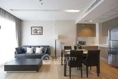 Modern living room with open kitchen, sleek furniture, and natural lighting.