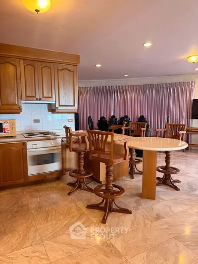Spacious kitchen with wooden cabinets and dining area, featuring elegant marble flooring and modern lighting.