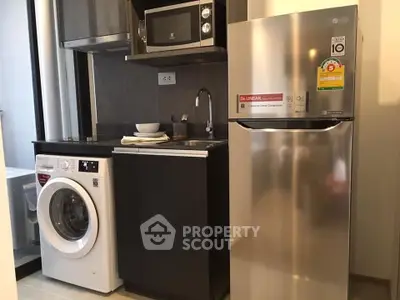Modern kitchen with washing machine, fridge, and microwave in compact layout.
