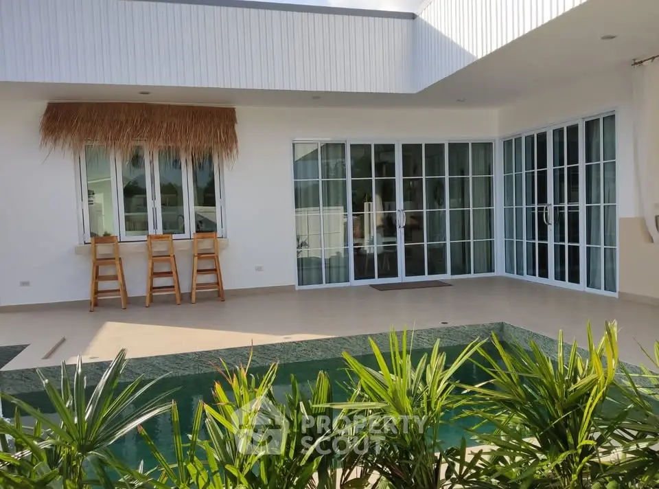 Modern villa with private pool and lush greenery, featuring large glass doors and a stylish outdoor bar area.