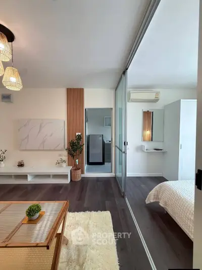 Modern living room with sliding glass doors leading to a cozy bedroom, featuring stylish decor and wooden flooring.