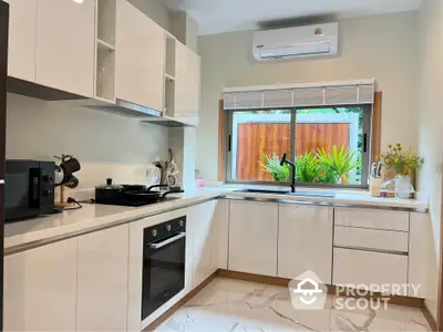 Modern kitchen with sleek white cabinetry and built-in oven, featuring a large window with garden view.