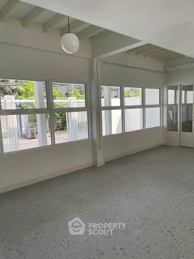 Spacious and bright room with large windows and modern lighting, perfect for versatile living or office space.