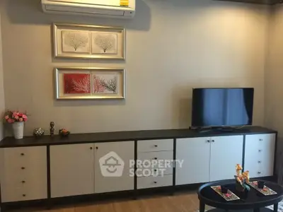 Modern living room with sleek cabinetry and wall-mounted TV, featuring elegant decor and air conditioning.