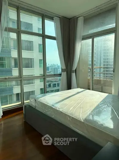 Spacious bedroom with large windows offering stunning city views in a modern high-rise apartment.