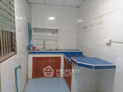 Compact kitchen with blue tiled countertops and white tiled walls, featuring a small sink and wooden cabinets.