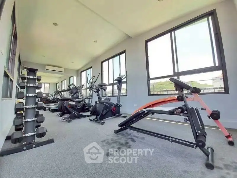Modern gym with exercise equipment and large windows in a residential building.