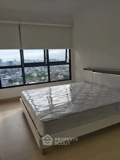 Spacious bedroom with large window offering stunning city views, featuring a modern bed frame and natural light.